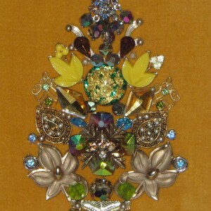 May include: A gold, green, and yellow jeweled Christmas tree ornament with a variety of rhinestones and beads.