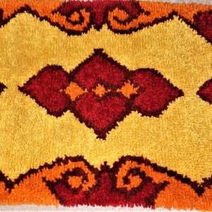 May include: A vintage shag rug with a geometric design in shades of orange, yellow, and red.
