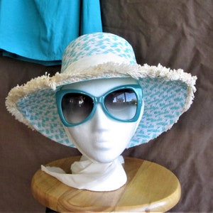 May include: A turquoise and white patterned sun hat with a frayed brim and a pair of turquoise sunglasses.