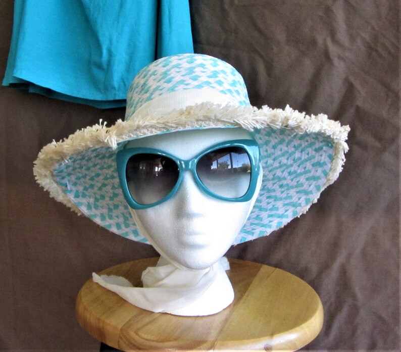 May include: A turquoise and white patterned sun hat with a frayed brim and a pair of turquoise sunglasses.