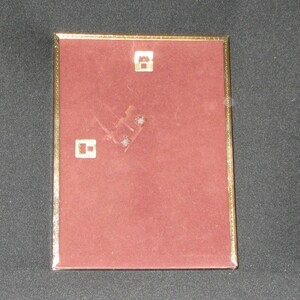 May include: A gold-colored picture frame with a red velvet backing. The frame has two small metal hooks on the back for hanging.