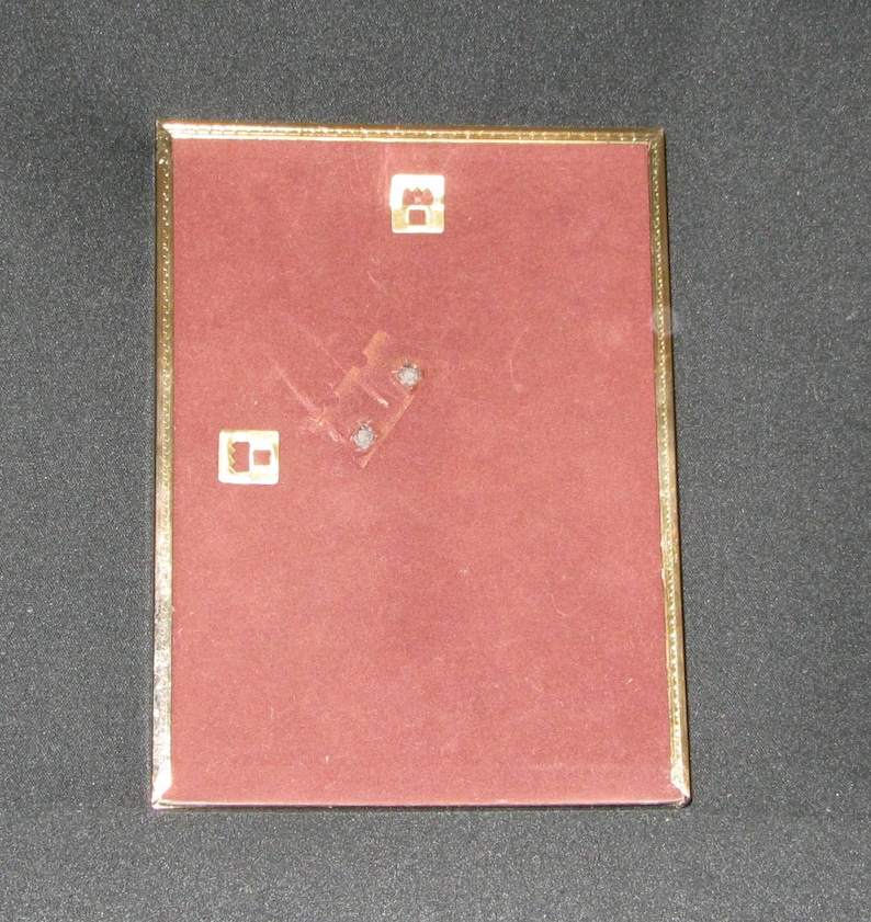 May include: A gold-colored picture frame with a red velvet backing. The frame has two small metal hooks on the back for hanging.