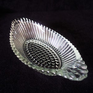 Puede incluir: Un plato ovalado de vidrio transparente con un diseño texturizado y acanalado. El plato tiene un patrón circular elevado en el centro.