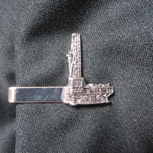 May include: Silver tie clip featuring a detailed model of an oil rig.