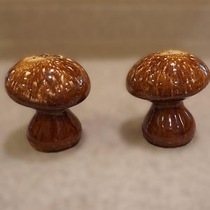 Puede incluir: Un juego de dos saleros y pimenteros de cerámica marrón en forma de hongo. Los saleros tienen un esmalte moteado y un acabado brillante.