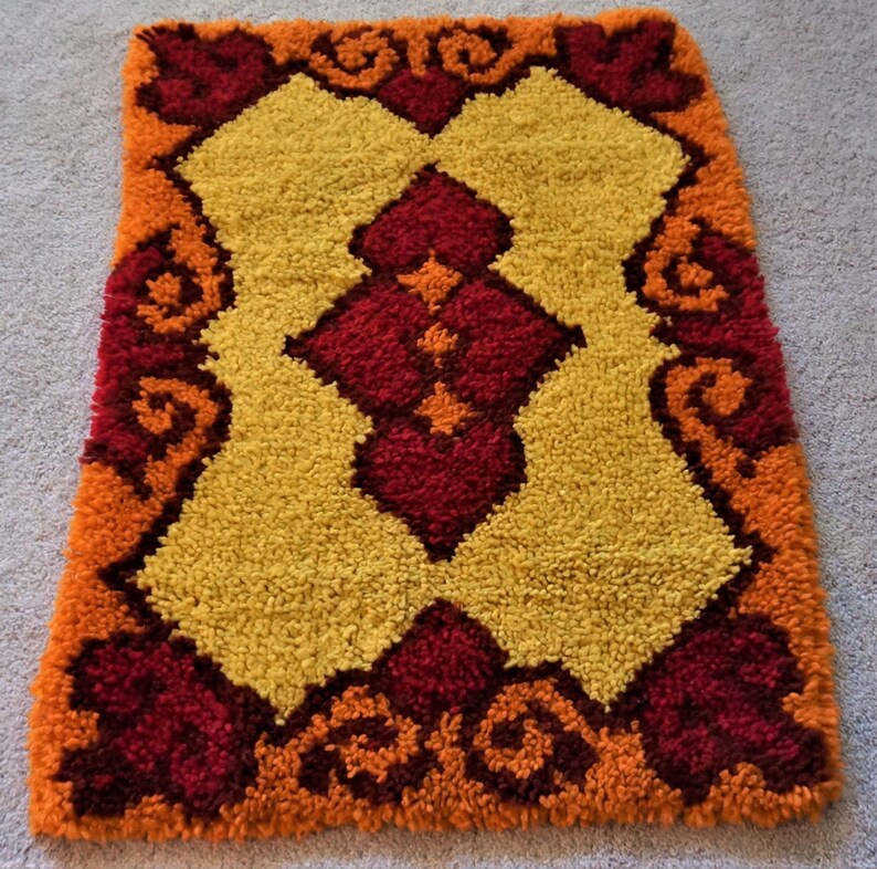 May include: A small, rectangular rug with a geometric pattern in shades of orange, yellow, and red. The rug has a fringed edge and is made of a soft, plush material.