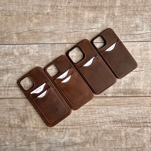 Op de afbeelding: Vier bruine leren telefoonhoesjes met een kaartslot aan de achterkant. Elk hoesje heeft een witte kaart met de tekst "CREDIT CARD" erop gedrukt.