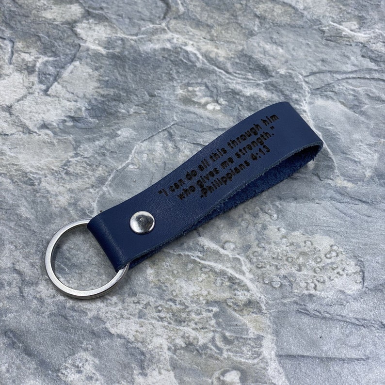 Peut inclure: Un porte-cl&eacute;s en cuir bleu fonc&eacute; avec un anneau de cl&eacute; en argent. Le porte-cl&eacute;s porte la gravure suivante : "Je peux tout faire par celui qui me donne de la force." - Philippiens 4:13.