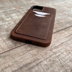 Op de afbeelding: Een bruine leren telefoonhoes met een flap om kaarten in op te bergen. De hoes heeft een gestikte rand en een verweerde look.