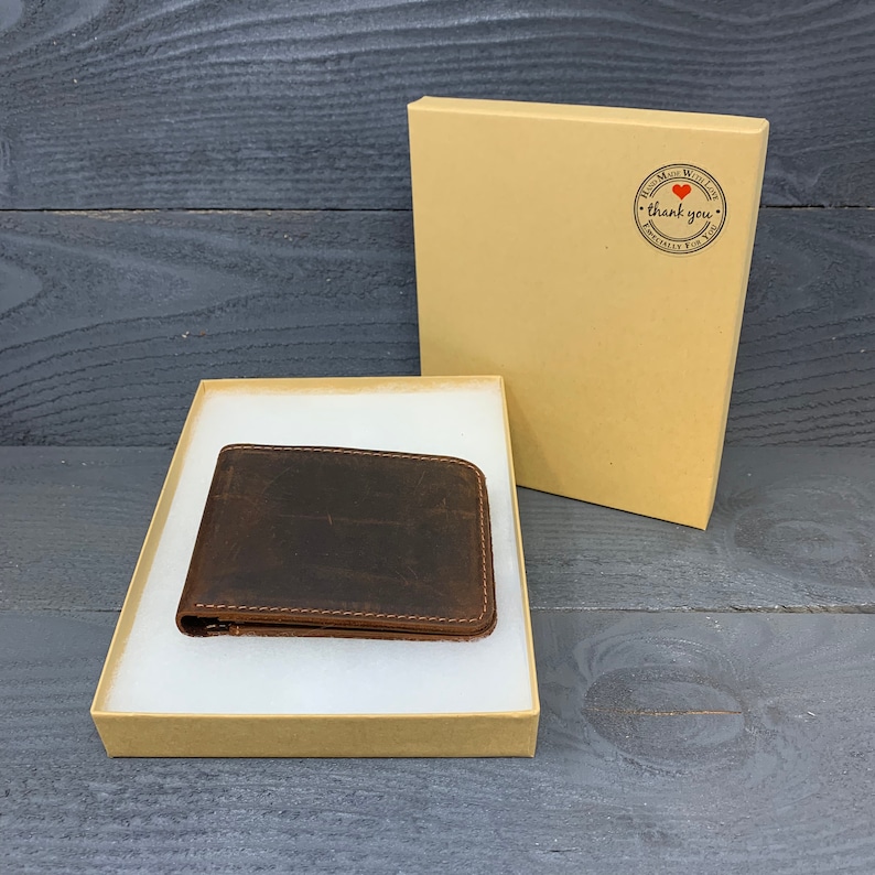 May include: A brown leather wallet in a cardboard box with a white interior. The box has a sticker that says "Hand Made With Love - Thank You - Especially For You".