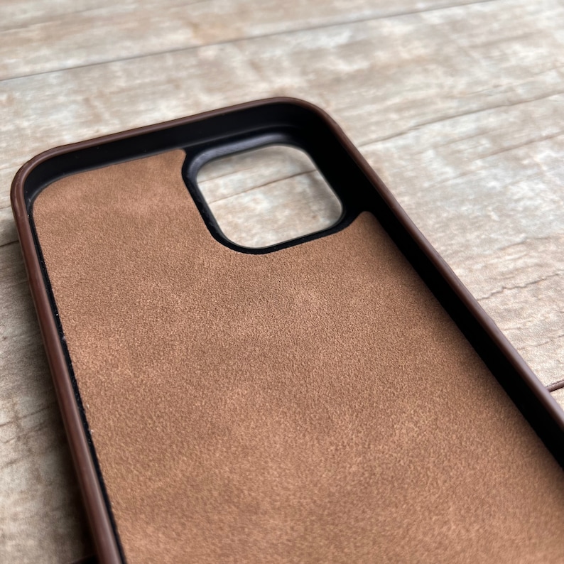 Op de afbeelding: Een bruine leren telefoonhoes met een su&egrave;de binnenkant. De hoes heeft een uitsparing voor de camera.
