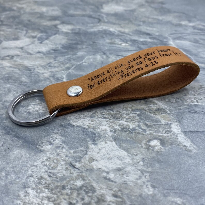 Peut inclure: Un porte-cl&eacute;s en cuir marron avec un anneau de cl&eacute; en argent. Le porte-cl&eacute;s porte la gravure suivante : "Above all else, guard your heart. For everything you do flows from it. -Proverbs 4:23".