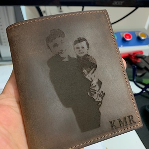 May include: A brown leather wallet with a personalized engraved image of two people and the initials "KMR".