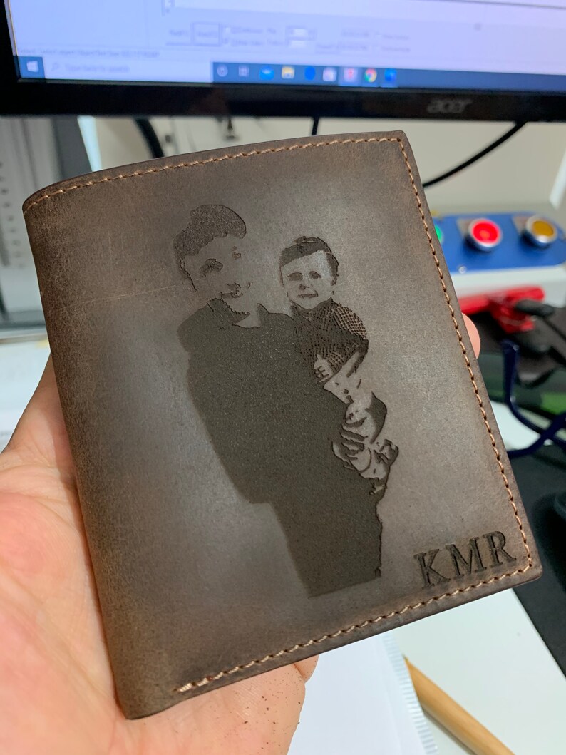 May include: A brown leather wallet with a personalized engraved image of two people and the initials "KMR".