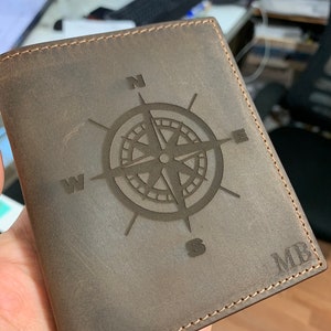 May include: A brown leather wallet with a compass design and the initials "MB" embossed on the front.