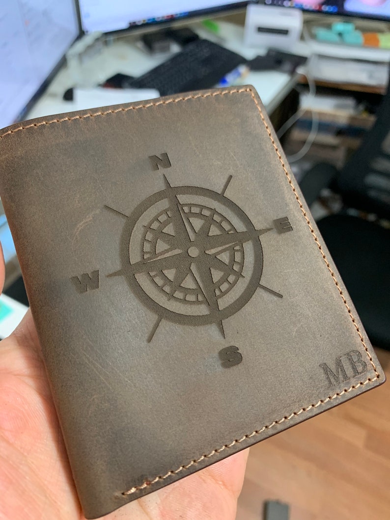 May include: A brown leather wallet with a compass design and the initials "MB" embossed on the front.