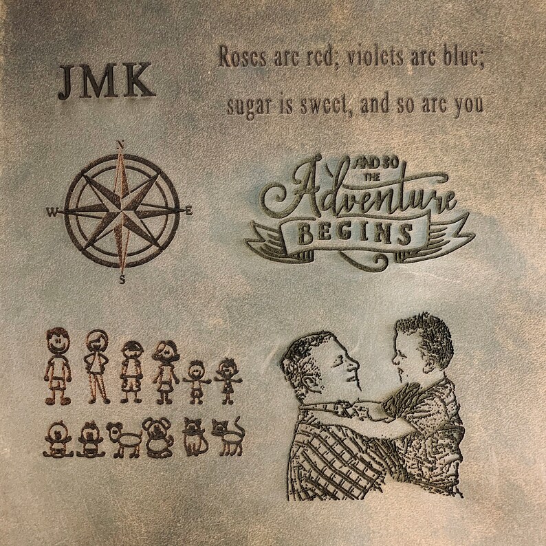 May include: A brown leather journal with the initials "JMK" embossed on the front cover. The journal also features a compass, a family of stick figures, and a father and son embracing. The text "And so the adventure begins" is embossed on the cover. The journal has a quote about roses, violets, sugar, and sweetness.