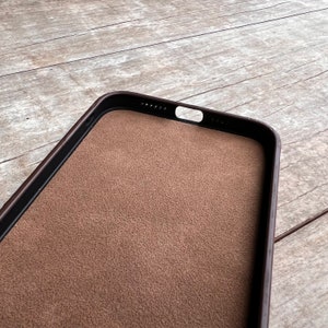 Op de afbeelding: Een bruine leren telefoonhoes met een zwarte rand. De hoes heeft een zachte, su&egrave;de-achtige voering.