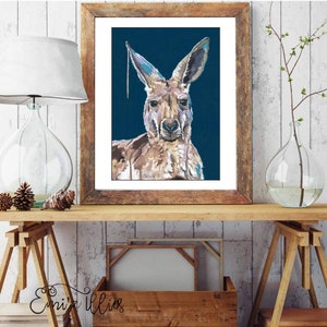 May include: A framed painting of a kangaroo with a blue background. The kangaroo is painted in a realistic style with brown, tan, and white fur. The painting is framed in a rustic wooden frame.