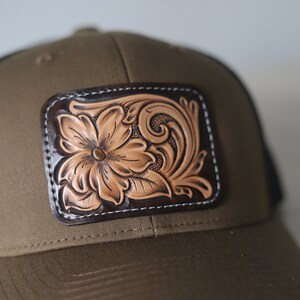 May include: A brown and black trucker hat with a leather patch featuring a tooled floral design.
