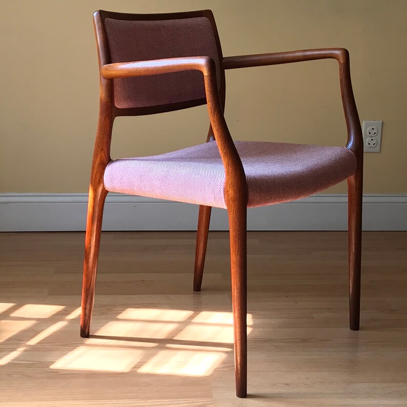 Peut inclure: Une chaise de style moderne du milieu du si&egrave;cle avec un si&egrave;ge en tissu rose clair et une structure en bois fonc&eacute;. La chaise a un dossier et des accoudoirs incurv&eacute;s.