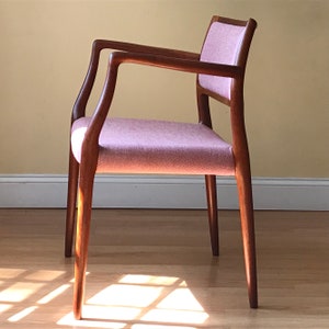 Peut inclure: Une chaise de style moderne du milieu du si&egrave;cle avec un si&egrave;ge en tissu rose clair et une structure en bois fonc&eacute;. La chaise a un dossier et des accoudoirs incurv&eacute;s.
