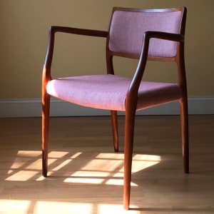Peut inclure: Une chaise de style moderne du milieu du si&egrave;cle avec un si&egrave;ge en tissu rose clair et une structure en bois fonc&eacute;. La chaise a un dossier et des accoudoirs incurv&eacute;s.