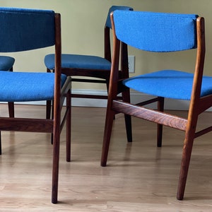 K&ouml;nnte beinhalten: Vier Esszimmerst&uuml;hle im Stil der Moderne der Jahrhundertmitte mit dunklen Holzrahmen und blauer Stoffpolsterung. Die St&uuml;hle haben ein schlichtes, elegantes Design mit einer leicht geschwungenen R&uuml;ckenlehne.