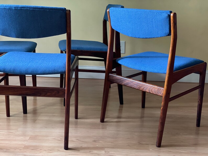 K&ouml;nnte beinhalten: Vier Esszimmerst&uuml;hle im Stil der Moderne der Jahrhundertmitte mit dunklen Holzrahmen und blauer Stoffpolsterung. Die St&uuml;hle haben ein schlichtes, elegantes Design mit einer leicht geschwungenen R&uuml;ckenlehne.