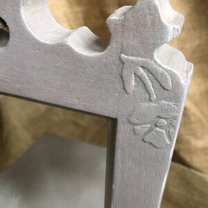 May include: Close-up of a gray, ornate picture frame corner. The frame features a floral design and decorative curves. The frame is painted in a muted gray color, with visible texture and slight wear.