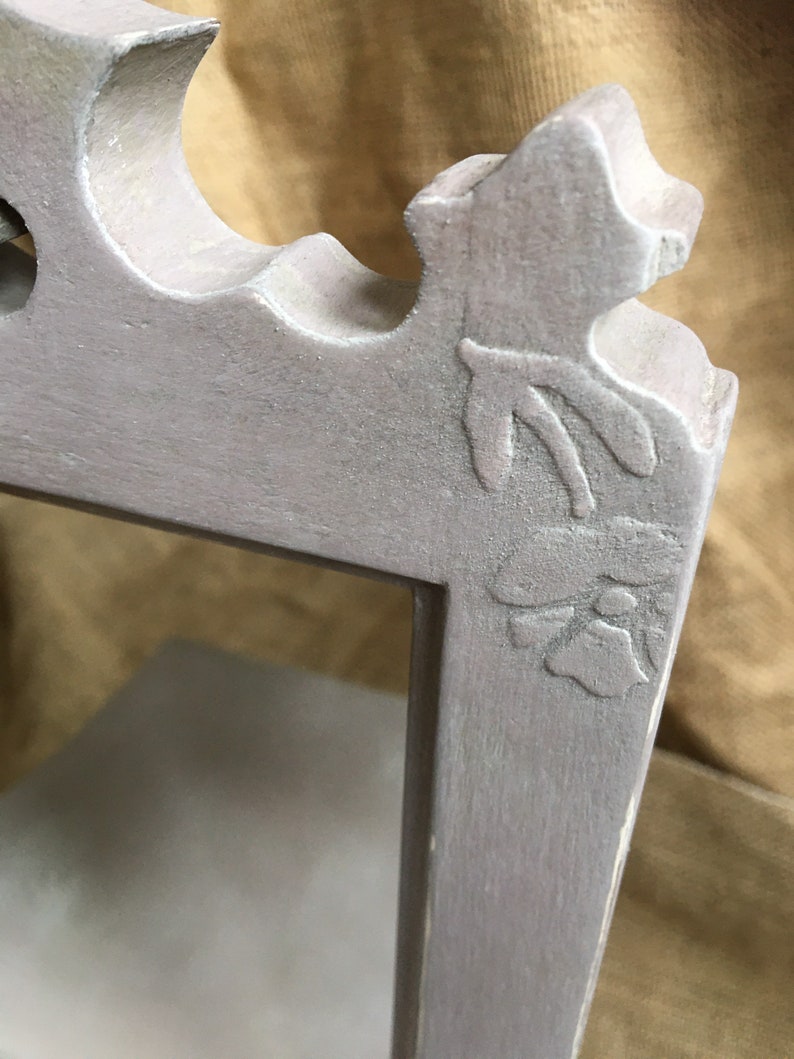 May include: Close-up of a gray, ornate picture frame corner. The frame features a floral design and decorative curves. The frame is painted in a muted gray color, with visible texture and slight wear.