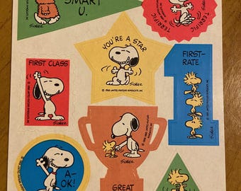Könnte beinhalten: Ein Bogen mit Vintage-Snoopy-Aufklebern. Die Aufkleber zeigen Snoopy in verschiedenen Posen, zusammen mit Sätzen wie "Smart U", "You're a Star" und "Great Job". Die Aufkleber sind in verschiedenen Formen und Farben.