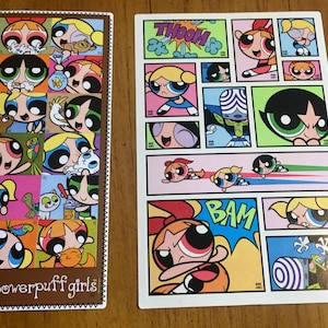 Puede incluir: Un conjunto de dos pegatinas de las Chicas Superpoderosas. La primera pegatina es una hoja rectangular con un borde marrón y 16 pegatinas individuales de las Chicas Superpoderosas en varias poses. La segunda pegatina es una hoja rectangular más grande con un fondo blanco y 10 pegatinas individuales de las Chicas Superpoderosas en varias poses. El texto "The Powerpuff Girls" está impreso en la primera pegatina.