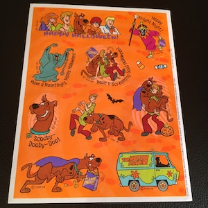 May include: A sheet of stickers featuring Scooby-Doo and the gang in various Halloween-themed scenes. The stickers are on an orange background with the text "Happy Halloween!" at the top. The stickers include Scooby-Doo dressed as a ghost, Scooby-Doo riding a skateboard, and the Mystery Machine.
