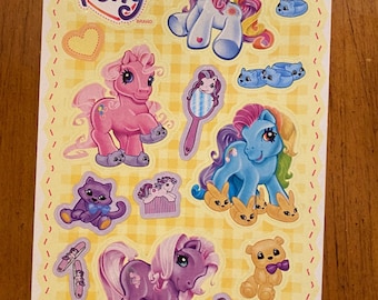 May include: A sheet of stickers featuring My Little Pony characters. The sheet is yellow with a checkered pattern and features 68 stickers of ponies, kittens, bunnies, and other accessories. The text "My Little Pony" is printed in a pink heart shape at the top of the sheet. The text "4 Sheets/Feuilles" is printed in the bottom left corner and "68 Stickers per package/ Autocollants par paquet" is printed in the bottom center. The text "2003 Hasbro" is printed in the bottom right corner.
