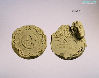 Könnte beinhalten: Zwei runde Resin-Sockel mit 40 mm Durchmesser für Miniaturenspiele. Ein Sockel zeigt ein Fleur-de-lis-Design mit einem kreisförmigen Rand und dem Text "NON NOBIS DOMINE". Der andere Sockel zeigt ein Design aus zerbrochenem Stein mit einem geformten menschlichen Kopf und dem Text "NON NOBIS DOMINE".