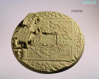Könnte beinhalten: Eine 100 mm runde Resin-Base für Miniaturen-Wargaming. Die Base verfügt über ein detailliertes Design eines Steinbodens mit einem zentralen Quadrat, das ein Fleur-de-lis-Muster und eine Inschrift in einer nachgebildeten mittelalterlichen Schrift zeigt. Die Inschrift lautet: "REGNANTE DEI GRACIA REX NOSTRUM IN HOC LOCO PROHIBITUR MORS ET SERVITUT PATRIAM NOSTRAM".