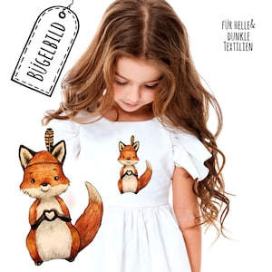 Könnte beinhalten: Ein Bügelbild mit einem niedlichen Comic-Fuchs, der ein Kopfschmuck trägt und ein Herz hält. Der Fuchs ist braun, orange und weiß. Der Text "Für helle & dunkle Textilien" befindet sich in der oberen rechten Ecke des Bildes.