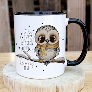 Puede incluir: Taza de cerámica blanca con borde y asa negros. La taza presenta una ilustración de dibujos animados de un búho con una bufanda y sentado en una rama con nieve. El texto en la taza dice "Die Welt ist schon weil Du drauf bist".