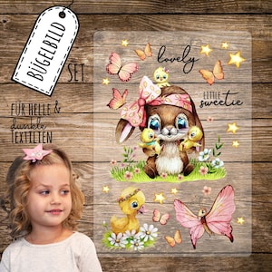 Könnte beinhalten: Bügelbild-Set mit einem niedlichen Hasen, der zwei Küken hält, einem Entenküken mit einer Blumenkrone und Schmetterlingen. Der Text "lovely little sweetie" ist im Design enthalten.
