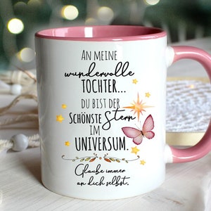 Könnte beinhalten: Weiße Keramiktasse mit rosafarbenem Rand und Henkel. Die Tasse hat eine Botschaft, die lautet "An meine wundervolle Tochter... Du bist der schönste Stern im Universum. Glaube immer an dich selbst."