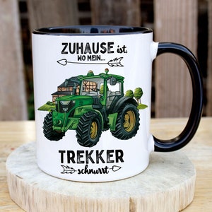 May include: White ceramic mug with a black handle. The mug has a green tractor illustration with the text "Zuhause ist wo mein... Trekker schnurrt" in black.