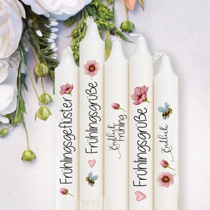 May include: Five white taper candles with floral and bee designs. Each candle has a different German phrase printed on it, including "Fr&uuml;hlingsgefl&uuml;ster" and "Fr&uuml;hlingsgr&uuml;&szlig;e". Pink flowers and a bee are also featured.