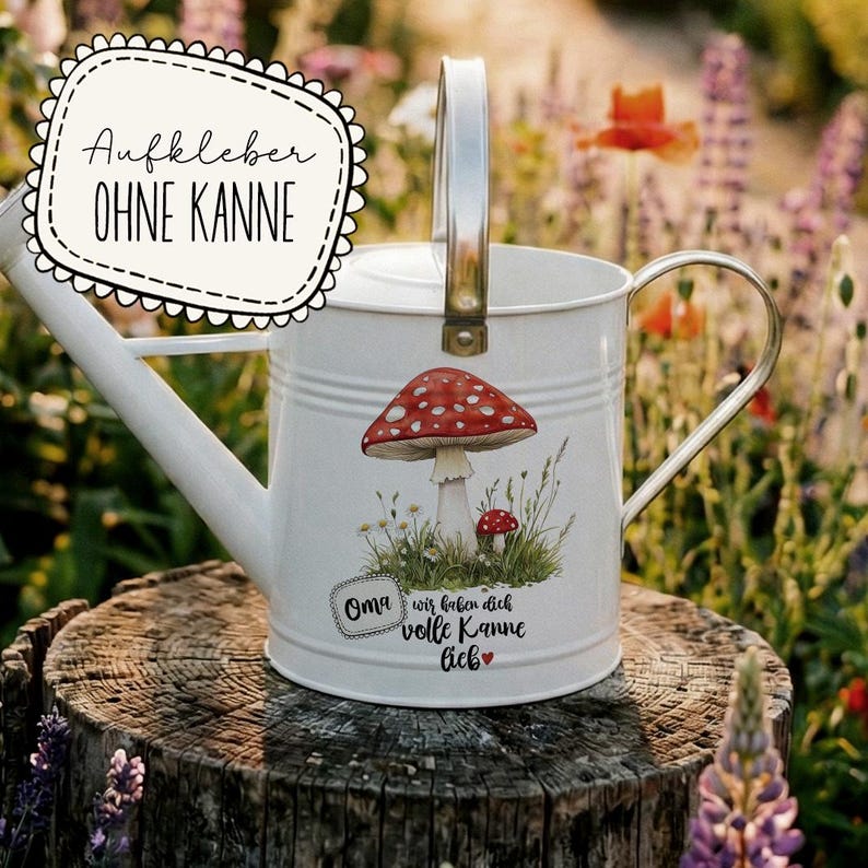 May include: White metal watering can with a silver handle and spout. The can features a red and white mushroom graphic and text in German. The watering can is sitting on a wooden stump in a garden setting.