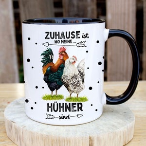 Könnte beinhalten: Weiße Keramiktasse mit schwarzem Henkel und schwarzem Rand. Die Tasse hat ein schwarz-weißes Punkte-Muster und zeigt einen Hahn und eine Henne mit dem Text "Zuhause ist wo meine Hühner sind".