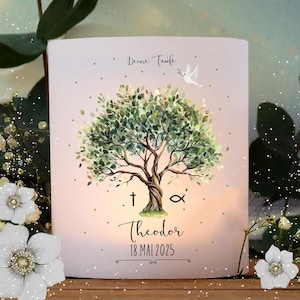 May include: A white candle with a watercolor illustration of a tree with green leaves and a dove flying above it. The text "Deine Taufe" is at the top of the candle, and the text "Theodor 18. Mai 2025" is at the bottom. The cross and the fish symbol are on either side of the name.