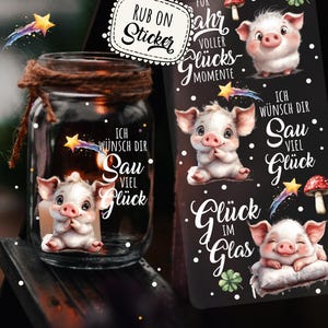 Könnte beinhalten: Ein Glas mit braunem Bindfaden, mit einem Schweineaufkleber und Text. Eine schwarze Karte mit Schweineillustrationen und deutschem Text befindet sich neben dem Glas. Das Glas und die Karte haben die Worte "Ich wünsch dir sau viel Glück".