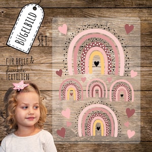 May include: A set of iron-on patches featuring pink, brown, and yellow rainbows with white polka dots and black outlines. The rainbows are arranged in a cascading pattern with hearts scattered around them. The text "Bügelbild SET" is visible in the top left corner of the image. The text "Für helle & dunkle TEXTILIEN" is visible in the bottom left corner of the image.