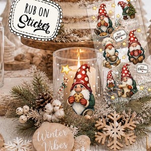 Könnte beinhalten: Ein Bogen mit Weihnachts-Wichtel-Aufreibebildern, die Wichtel mit rot-gepunkteten Mützen zeigen, die Kekse, Tassen oder Geschenke halten, mit Texten wie Merry Christmas und Fröhliche Weihnachten, neben einer Kerze mit einem Wichtel-Aufkleber.