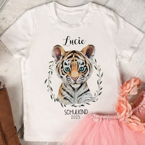 Può includere: Maglietta bianca con un'illustrazione di un cucciolo di tigre, una ghirlanda di foglie verdi e il testo "Lucie" e "Schulkind 2023".